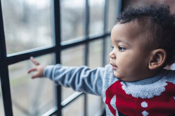 cute little Afro-American curly-haired boy looking through the window, medium closeup. High quality photo