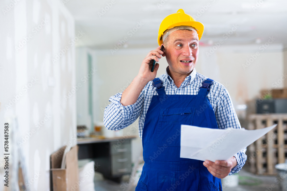 Wall mural Construction worker having telephone conversation about working plan in apartment.