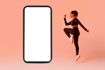 New workout app. Fitness black lady jumping near big cellphone with blank screen over peach background, mockup