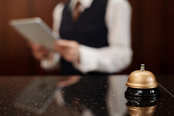 Selective focus on bell and reception counter against female manager in uniform using tablet while standing by her workplace in lounge