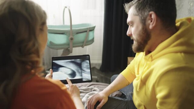 A pregnant couple looks at a picture of a baby on an ultrasound scan. Happy parents-to-be laugh and rejoice. High quality 4k footage