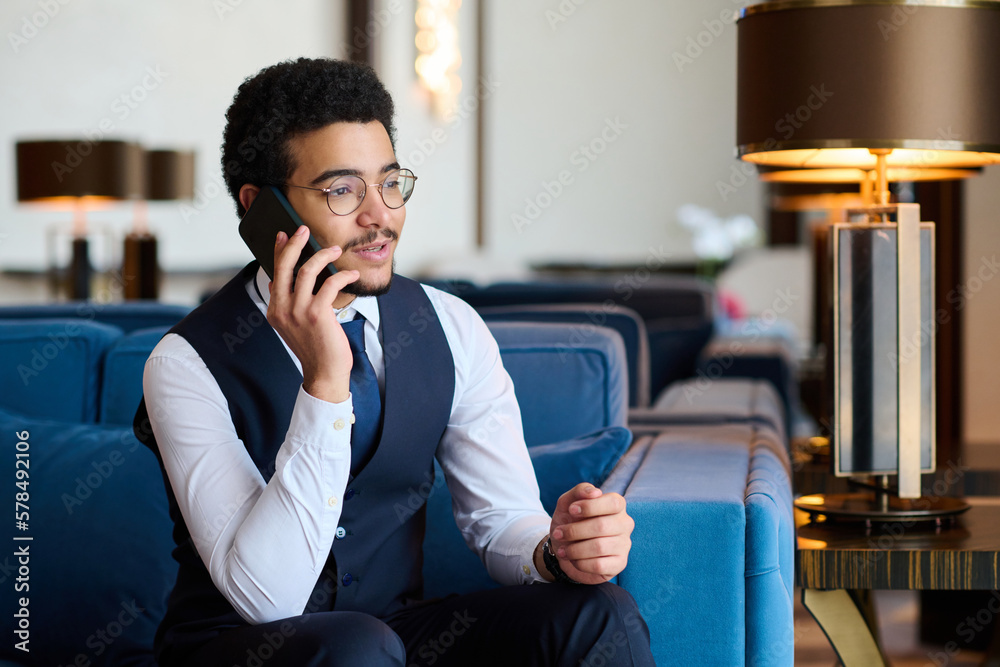 Aufkleber young confident businessman in formalwear talking to colleague or client on smartphone while sitting