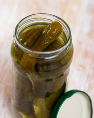 Glass bottle of marinated cucumbers on wooden background