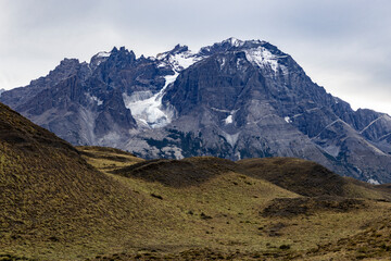 Snowy mountains behind grassy hills of Torres del Paine National Park in Chile, Patagonia, South America