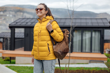 Young female in yellow down jacket walks outdoor near modular cabin houses