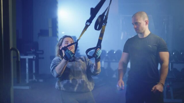 Woman doing fitness trx exercises in gym with trainer. Workout and active lifestyle. Professional personal sports trainer. Healthy Lifestyle . Athletic man and girl. High quality 4k footage