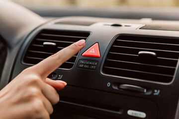 Close up woman press emergency gang red button accident, black dark car interior. Dashboard display panel, airbag icon inscription sign. Climate control. Electric, hybrid elegant modern vehicle
