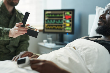 Focus on hand of soldier holding small open box with medal for defense of Motherland and showing it to injured soldier lying in hospital bed