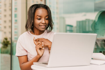 Happy positive smiling african american woman hipster sitting outside use laptop, excited triumph...