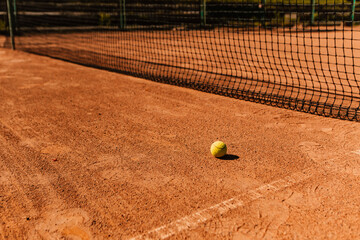 Light orange empty outdoor clay court surface dry grungy ground baseline detail for playing tennis with net in sunny day with yellow green ball, gravel texture background, copy space for text 
 - obrazy, fototapety, plakaty