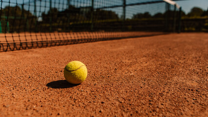 Light orange empty outdoor clay court surface dry grungy ground baseline detail for playing tennis with net in sunny day with yellow green ball, gravel texture background, copy space for text 

