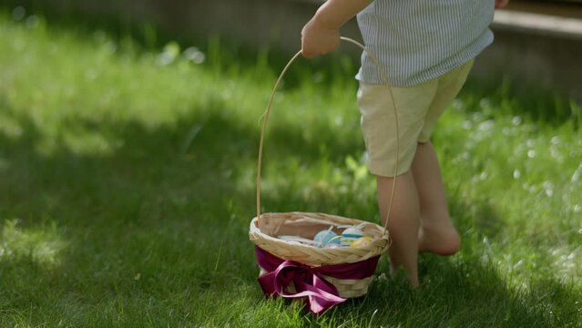 Happy Egg hunt Easter game outdoors. Barefoot child with basket in hands searching hidden Easter eggs in green grass. Traditional spring holiday. children spring activities outdoors