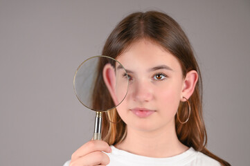 Young caucasian girl with magnifying glass over gray background with copy space. Teengirl showing her ear