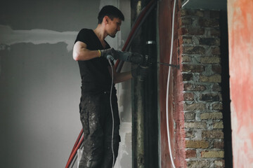 A young man breaks a wall with a perforator.