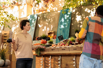 Young family talking to each other and buying healthy organic veggies at farmers market, local food stand. People customers shopping for fresh natural produce, looking at organic products.