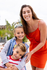 Portrait of happy biracial mother and children embracing and smiling at beach - obrazy, fototapety, plakaty