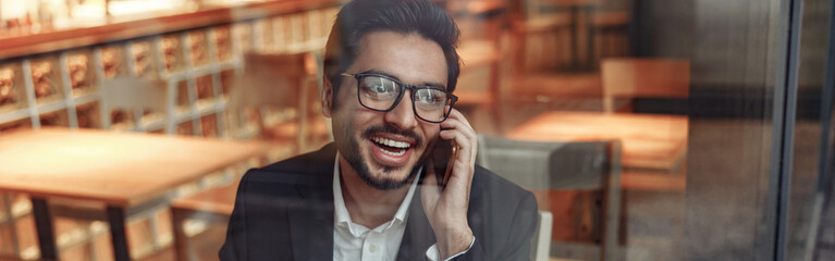 Smiling indian businessman is talking phone with client during lunch time in cozy cafe