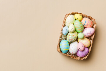 Colorful Easter eggs in wicker basket against colored background, closeup. top view with copy space