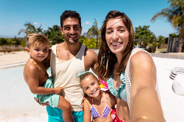 Happy biracial family taking selfie by the swimming pool - Powered by Adobe