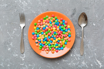 cutlery on table and sweet plate of candy. Health and obesity concept, top view on colored...
