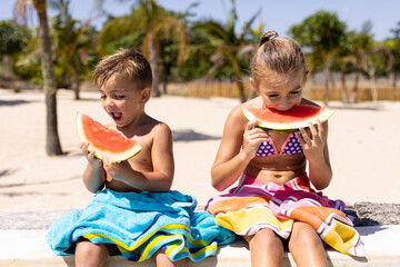 Fototapeta Happy biracial brother and sister eating watermelon by the swimming pool obraz
