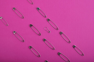 Beautiful even rows of silver safety pins in various sizes and shapes beautifully laid out on a bright pink textured background. Sewing accessories.