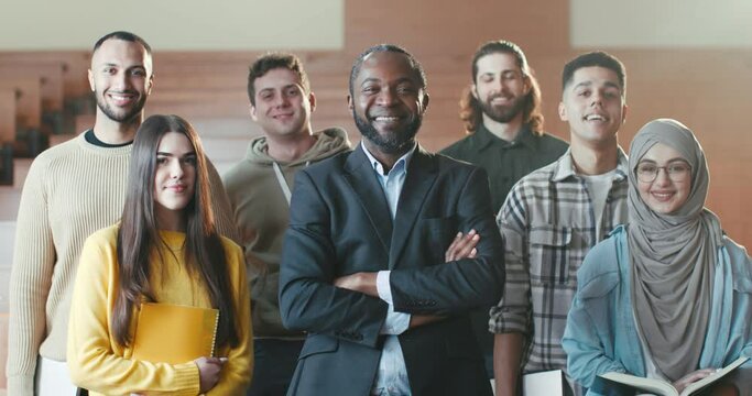 Portrait shot of African American male happy professor among mixed-races students in auditorium of University laughing n front of camera. Teacher and pupils concept. Posing for photo.