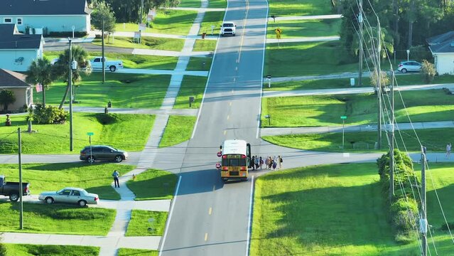 Top view of standard american yellow school bus picking up kids at rural town street stop for their lessongs in early morning. Public transport in the USA