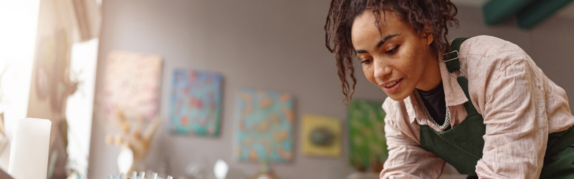 Smiling Woman decorator making green ikebana on tray in florist workshop. Blurred background - Powered by Adobe
