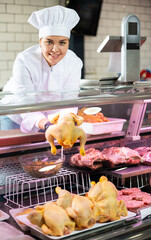 Happy female butcher holding whole chicken in meat section of supermarket