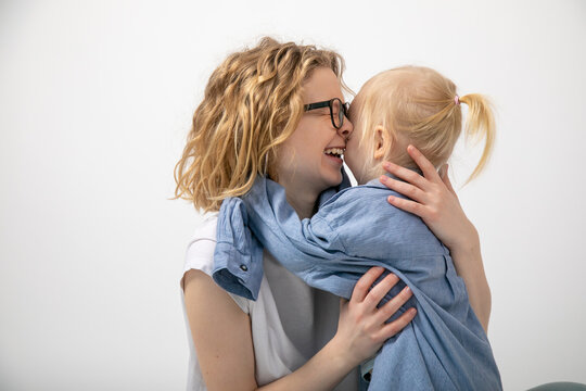 Charming red-haired woman in white T-shirt laughs happily hugging her daughter, who is wearing her mother's blue shirt.