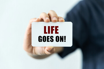 Life goes on text on blank business card being held by a woman's hand with blurred background. Business concept about life.