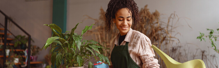 Smiling woman florist taking care of plant watering it in floral shop