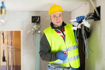 Experienced diligent electrician laying electric wires in building under construction