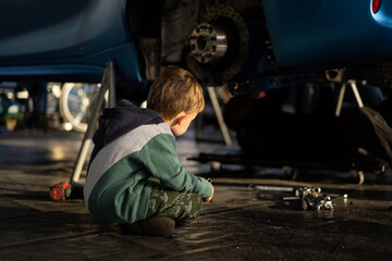 Little boy helps his dad in the garage to repair the car. Time with father.