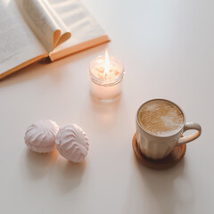 coffee cup, flower, candle and a book on a white table background top view. minimal home interior decor