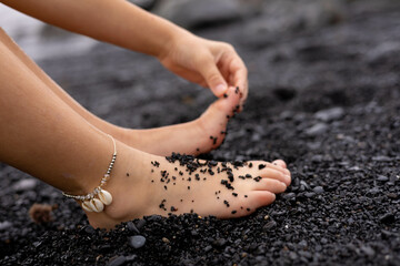 Two kid feet in the beach with black sand because of a volcano in Tenerife, Canary islands, and a hand touching one of them