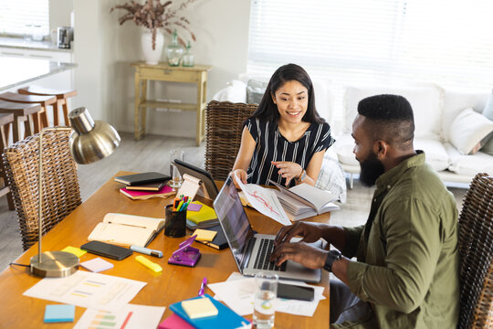 Smiling diverse friends working together at home, using laptop