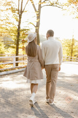 Fototapeta premium Back view of a couple lovers walking holds hands in the park at sunset. Love, youth, happiness concept. Lovely romantic moment between young man and woman in love. Happy family.