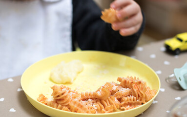 Two years old baby eating pasta with tomato sauce