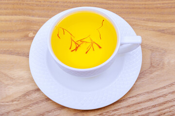 Saffron tea in a white cup on wooden background. A fragrant healthy drink.