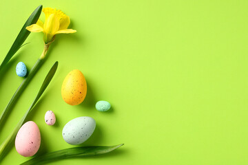 Happy Easter banner design. Daffodil flowers and colorful Easter eggs on green background. Flat lay, top view.