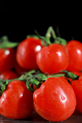 close up of bunch of fresh cherry tomatoes with green stems isolated on dark grey background