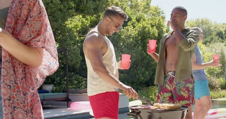 Happy diverse group of friends having bbq and drinking drinks at pool in summer