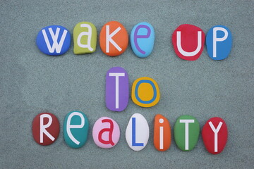 Wake up to reality, motivational slogan composed with multi colored stone letters over green sand