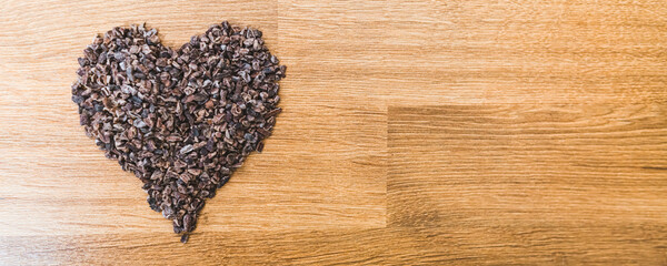 Roasted cocoa beans forming a heart shape on wooden table. High angle view. Wide shot. Copy space idea. High quality photo