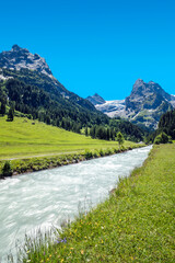 Green grass area and river with Alps moutain under blue sky, from Switzerland