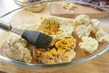Raw cauliflower slices in a glass casserole are coated with a mixture of spices, herbs and olive...