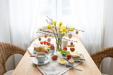 Breakfast for two with daffodils and Easter decoration on a wooden table at the window, copy space, selected focus