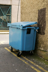 Small wheelie bin in an alley or street ready for collection. Rubbish disposal and management in a city.